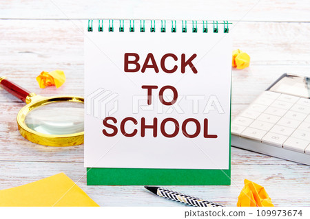 Back to school text on the white sheet of the notebook is next to a magnifying glass, calculator, pencil, stickers 109973674