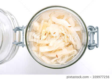 German sauerkraut, in an opened swing top glass jar. Cut raw cabbage, fermented by lactic acid bacteria. Traditionally a warm served side dish, flavored with juniper berries and caraway seeds. Photo. 109977256