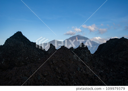 Landscape view of Mount Abang in the background through solidified black volcanic lava of an active volcano Batur, Bali island. Landscape view of Mount Abang in the background through solidified black volcanic lava of an active volcano Batur, Bali island. 109979379