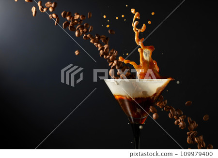 Espresso Martini drink with splashes and falling coffee beans on a black background. Espresso Martini drink with splashes and falling coffee beans on a black background. 109979400