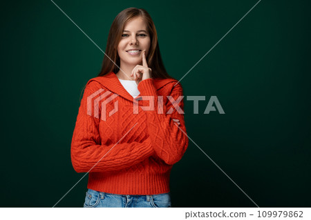 Smiling young woman with brown straight hair wearing a red sweater on a green background with copy 109979862