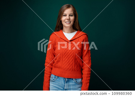 Beautiful young woman with brown hair wearing a red sweater on a green background 109980360