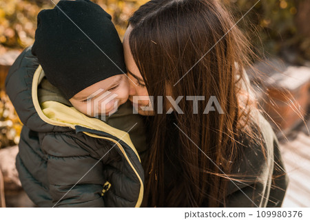 Happy loving young mother kisses her toddler son on the walk Happy loving young mother kisses her toddler son on the walk 109980376