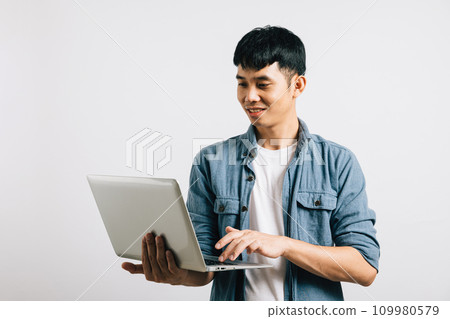 Portrait of confident Asian businessman, smiling and typing on a laptop keyboard, engaged in a successful online email or chat isolated on white background, showcasing his enthusiasm for technology. Portrait of confident Asian businessman, smiling and typing on a laptop keyboard, engaged in a successful online email or chat isolated on white background, showcasing his enthusiasm for technology. 109980579