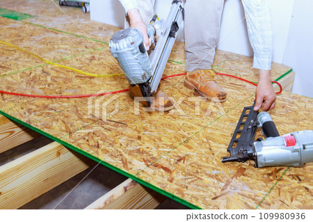 New home flooring is installed with wooden plywood using an air nail gun New home flooring is installed with wooden plywood using an air nail gun 109980936
