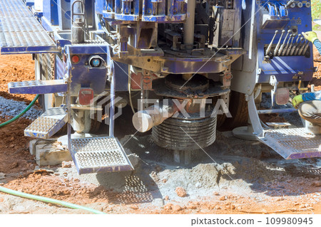 This water well is being dug in suburban yard by workmen using drilling machine to obtain artesian water. 109980945