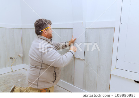 During installation of wooden trim moldings in room contractor nails wood with nails using air gun During installation of wooden trim moldings in room contractor nails wood with nails using air gun 109980985