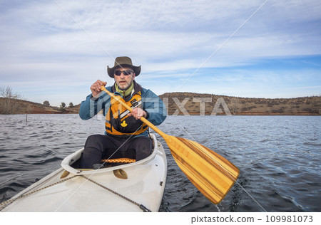 senior male in life jacket is paddling expedition canoe, cold season scenery on Horsetooth Reservoir in northern Colorado, POV from action camera senior male in life jacket is paddling expedition canoe, cold season scenery on Horsetooth Reservoir in northern Colorado, POV from action camera 109981073