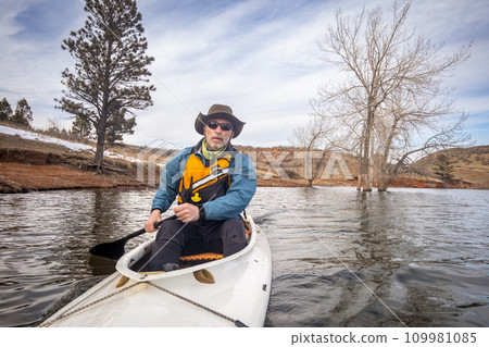 senior male in life jacket is paddling expedition canoe, cold season scenery on Horsetooth Reservoir in northern Colorado, POV from action camera 109981085