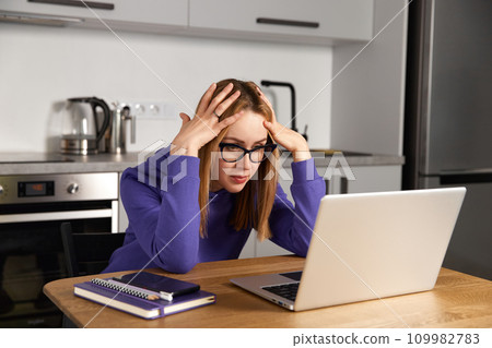Annoyed young adult woman in glasses work study at kitchen using laptop. Remote education 109982783