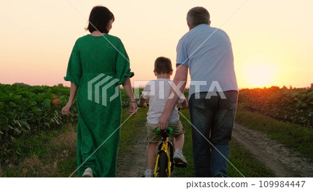 Parents teach son riding bicycle on plantation road in summer on vacation Parents teach son riding bicycle on plantation road in summer on vacation 109984447