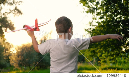 Happy child holds toy airplane model on vacation in countryside at sunset Happy child holds toy airplane model on vacation in countryside at sunset 109984448