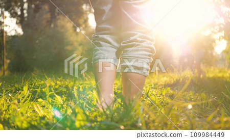 Eager son runs without shoes across lawn in meadow during summer sunset Eager son runs without shoes across lawn in meadow during summer sunset 109984449