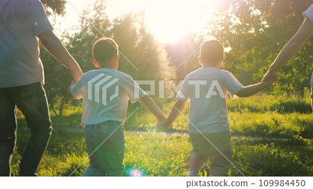 Substantial family of parents and children runs hand in hand across meadow Substantial family of parents and children runs hand in hand across meadow 109984450