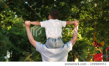 Dad carries joyful infant boy on shoulders having time together in city park 109984451