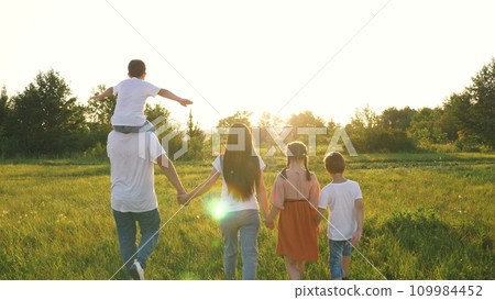 Cheerful family with children raises up hands walking across field at sunset 109984452