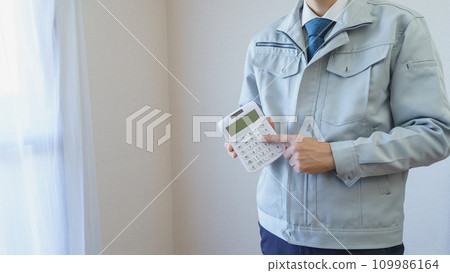 A man in work clothes holding a calculator inside an apartment | Renovation survey/estimate image A man in work clothes holding a calculator inside an apartment | Renovation survey/estimate image 109986164