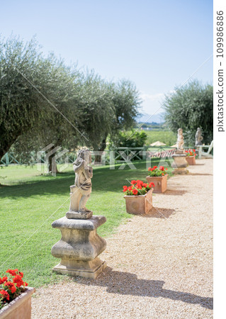 Stone sculptures in a green garden near flowering pots Stone sculptures in a green garden near flowering pots 109986886