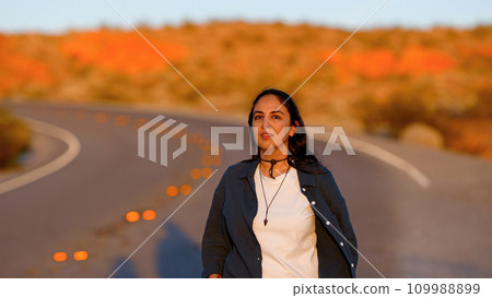 Young Woman walking down a desert road at sunset Young Woman walking down a desert road at sunset 109988899