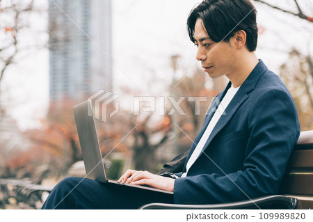 A man using a computer on a park bench A man using a computer on a park bench 109989820
