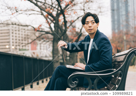 A man using a computer on a park bench A man using a computer on a park bench 109989821