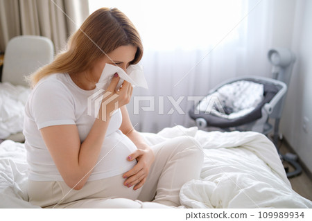 A pregnant woman blows her nose while sitting on the bed. Colds during pregnancy.  109989934