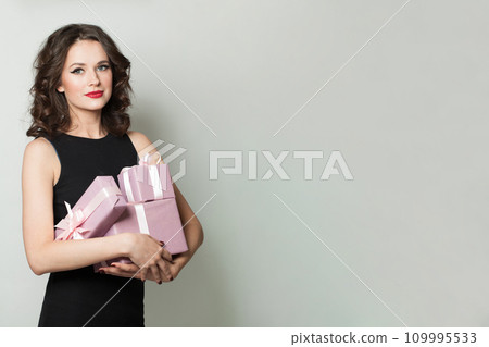 Cheerful woman with gift. Female model holding pink present box with silk ribbon on white background Cheerful woman with gift. Female model holding pink present box with silk ribbon on white background 109995533
