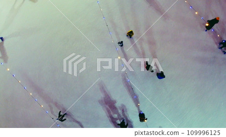 People skating on ice skating rink outdoors on winter night top view. Aerial drone view. Luminous glowing garlands lamps lighting. Cast long shadows. New Year Christmas celebration holidays recreation People skating on ice skating rink outdoors on winter night top view. Aerial drone view. Luminous glowing garlands lamps lighting. Cast long shadows. New Year Christmas celebration holidays recreation 109996125
