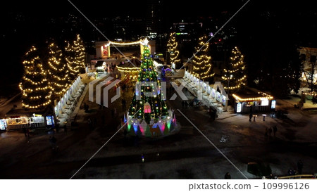 Many people skating on beautiful ice skating rink in open air decorated New Year Christmas illuminations, decorations, luminous garlands on winter night. New Year Christmas holiday celebration. Aerial 109996126