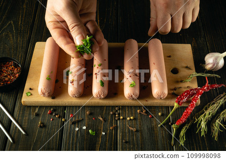 Adding parsley by hand to raw meat sausages before cooking. Concept of cooking delicious grilled sausages with spices and rosemary 109998098
