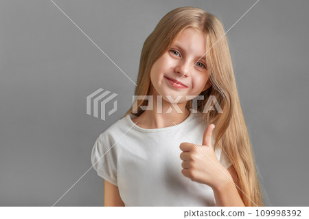Happy child, little girl showing thumbs up gesture in a white T-shirt 109998392