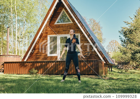 Sporty woman does breathing exercise on lawn of a country house 109999328