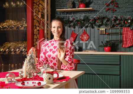 Happy woman sits behind the table decorated for Christmas Happy woman sits behind the table decorated for Christmas 109999353