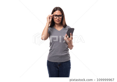 young positive brunette woman with glasses dressed in a gray t-shirt is studying a smartphone on a young positive brunette woman with glasses dressed in a gray t-shirt is studying a smartphone on a 109999967
