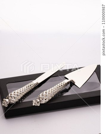 Wedding cake is set next to stainless steel utensil serving set for bride and groom to cut a slice of cake. 110000987