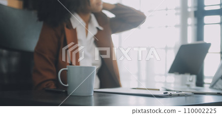 Asian women sitting in a home office With stress and eye strain.Tired businesswoman holding eyeglasses and massaging nose bridge. There are tablets, laptops, and coffee. 110002225