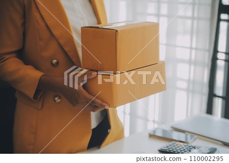 Startup SME small business entrepreneur of freelance Asian woman using a laptop with box Cheerful success happy Asian woman her hand lifts up online marketing packaging and delivery SME idea concept 110002295