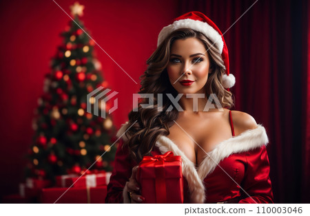 A woman dressed in a red Santa suit with a deep-cut design and white fur trim, is holding a red gift box in front of her. 110003046