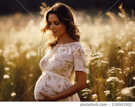 Tender young pregnant woman standing in a sunlit field, gently cradling her belly, a look of joy and anticipation on her face, surrounded by wildflowers 110003302