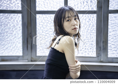 A young woman in a black dress relaxing by the window 110004009