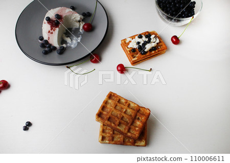 breakfast delicious snack two soft Belgian waffles lie on top of each other next to blueberries cherry cheese cottage cheese with space for text and with copyspace breakfast delicious snack two soft Belgian waffles lie on top of each other next to blueberries cherry cheese cottage cheese with space for text and with copyspace 110006611
