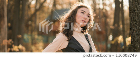 Banner portrait woman walking in autumn park, happy mood and fashion style trend and curly long brown hair copy space. Fall season and pretty female portrait copy space. Millennial generation concept 110008749