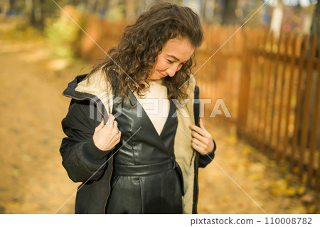 Attractive young woman walking in autumn park, happy mood and fashion style trend and curly long brown hair. Fall season and pretty female portrait copy space. Millennial generation concept 110008782
