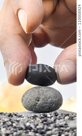 Hand of man places black stone on gray stone creating a pyramid, zen concept, vertical frame. 110008924
