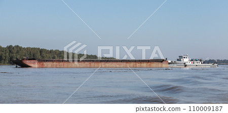 A pusher boat transports cargo barge along a river A pusher boat transports cargo barge along a river 110009187