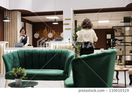 Hotel concierge checking record forms in lounge area at reception, reviewing registration files and booking bureaucracy. Female manager working on providing excellent service for guests. Hotel concierge checking record forms in lounge area at reception, reviewing registration files and booking bureaucracy. Female manager working on providing excellent service for guests. 110010329
