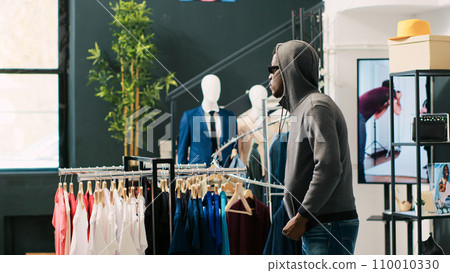 African american thief trying stole trendy clothes being caught by store security guard in clothing store. Asian bodyguard asking robber to return fashionable merchandise or will call the police 110010330