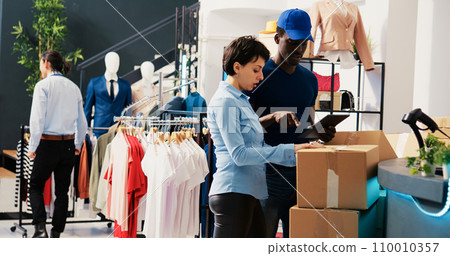 Store employees checking cardboard boxes, analyzing shipping report on tablet computer in shopping centre. Manager working at online customers orders, preparing packages for courier in modern boutique Store employees checking cardboard boxes, analyzing shipping report on tablet computer in shopping centre. Manager working at online customers orders, preparing packages for courier in modern boutique 110010357