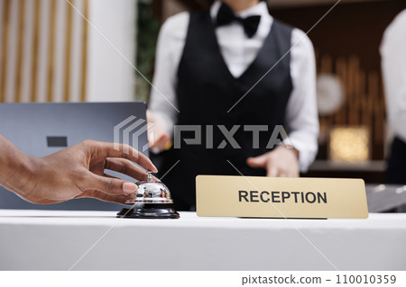 Tourist using service bell at front desk, ringing bell to talk to receptionist in lobby and check in. Hotel guest at reception counter receiving luxury assistance with room accommodation. Close up. 110010359