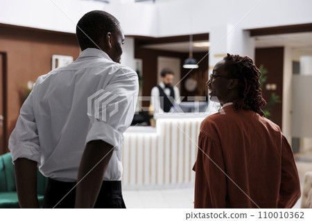 Guests arriving at hotel reception in lobby, entering lounge area and talking to receptionist about room reservation. Young couple asking front desk staff about accommodation and service. Guests arriving at hotel reception in lobby, entering lounge area and talking to receptionist about room reservation. Young couple asking front desk staff about accommodation and service. 110010362